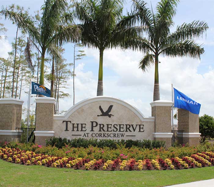 Entrance sign for The Preserve at Corkscrew residential community on Corkscrew Road, with landscaped flowers and palm trees, flanked by two flags labeled Pulte and Lennar in scenic Southwest Florida.