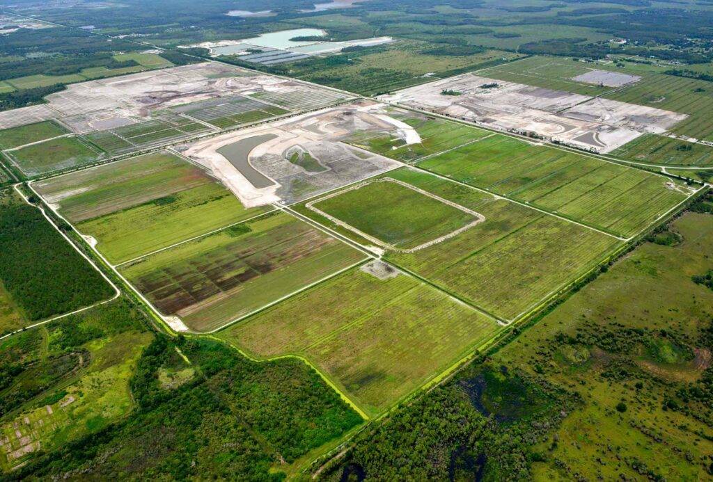 Aerial view of large farmland near Corkscrew Road in Southwest Florida, with green fields and several rectangular community plots under development, intersected by dirt roads.