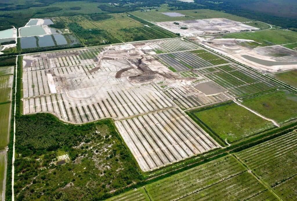Aerial view of a large construction site off Corkscrew Road in Southwest Florida, with cleared land, dirt roads, and green fields surrounding the growing community in this rural area.